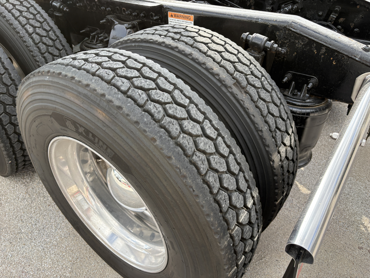 Dual rear truck tires on a Freightliner Cascadia 126 tractor showing tread pattern and chrome wheel, part of the chassis and exhaust nearby.