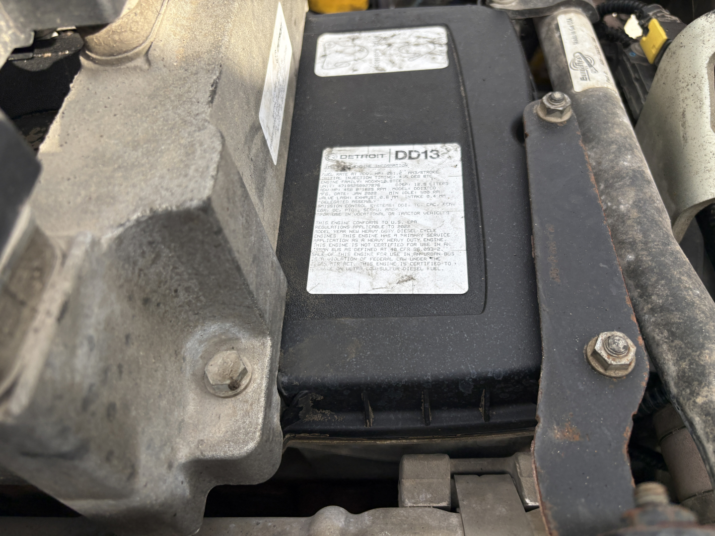 Engine bay showing a DD13 label on a rectangular black component with bolts and nearby labels, Freightliner CASCADIA 126 context.