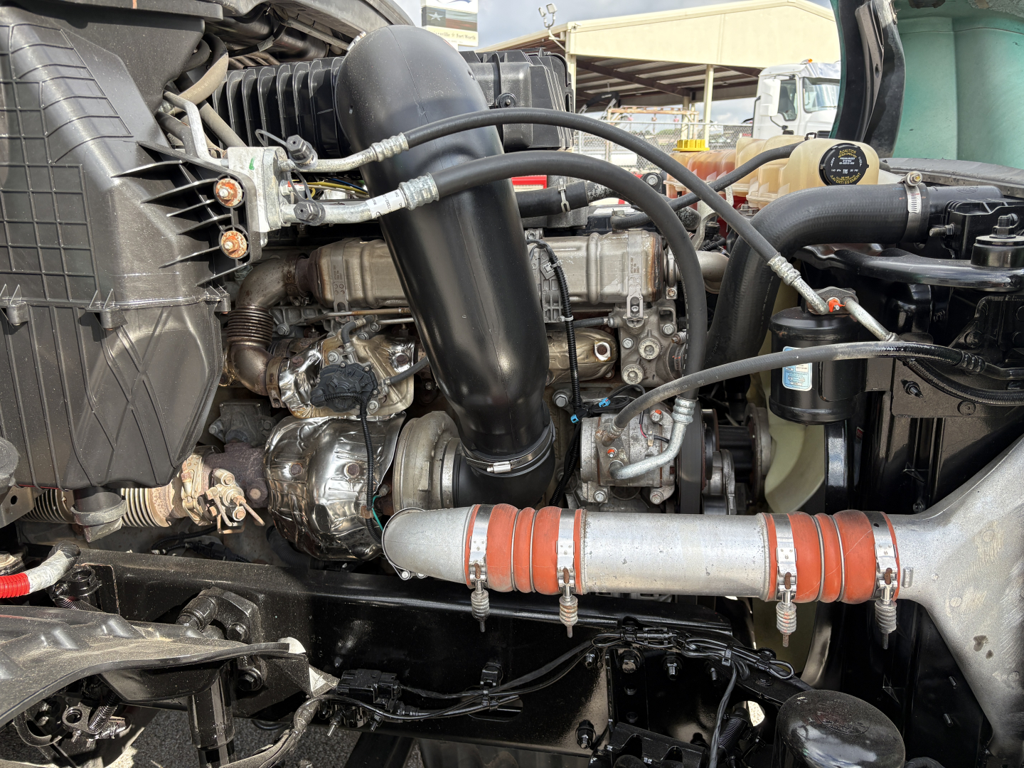 Engine bay of a Freightliner Cascadia 126 showing intake hose, intercooler piping, and various hoses with metal clamps.