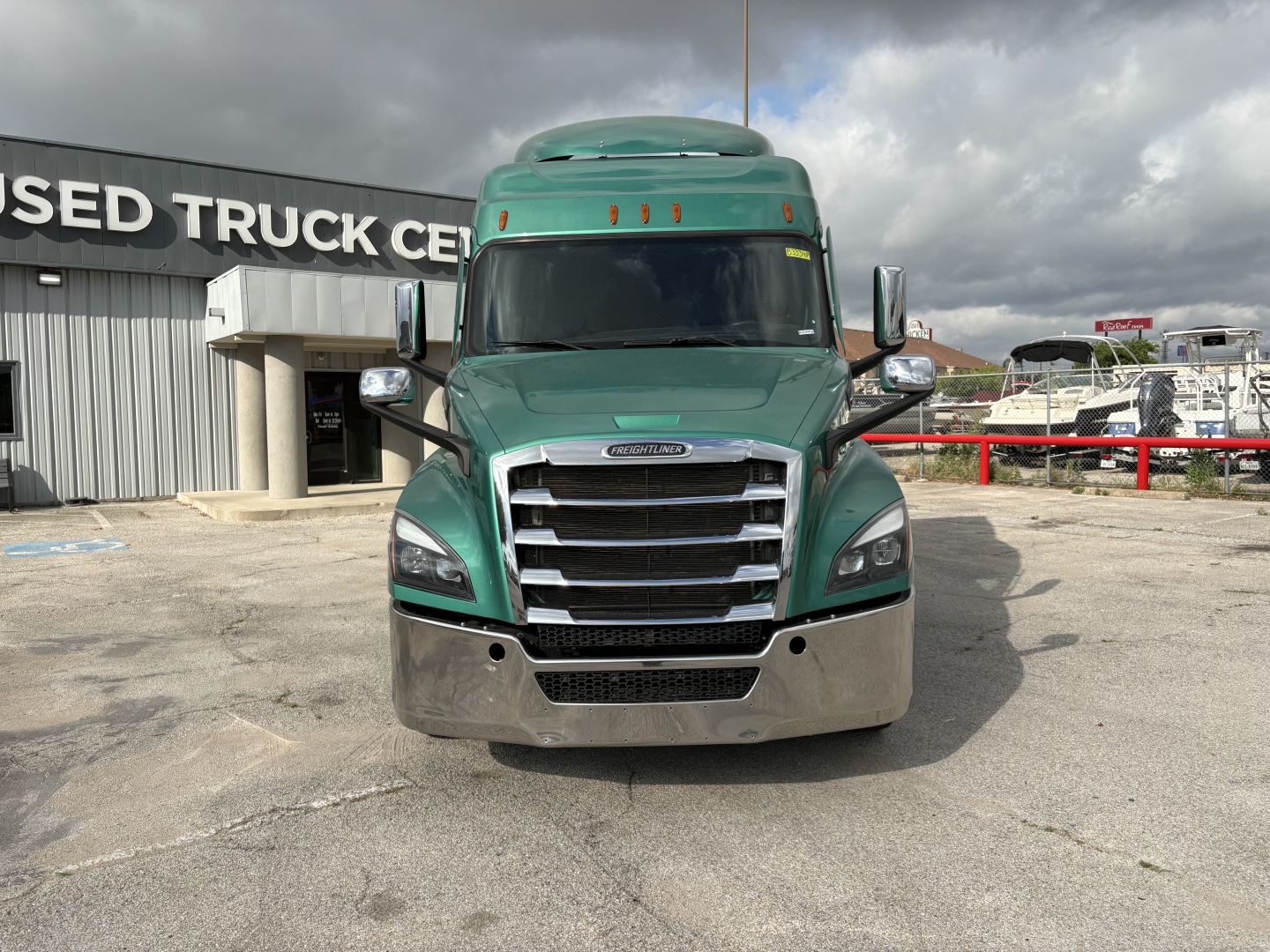 Truck front view of a green 2023 Freightliner Cascadia 126 with chrome grille and bumper, windshield, side mirrors, and cab roof fairing.