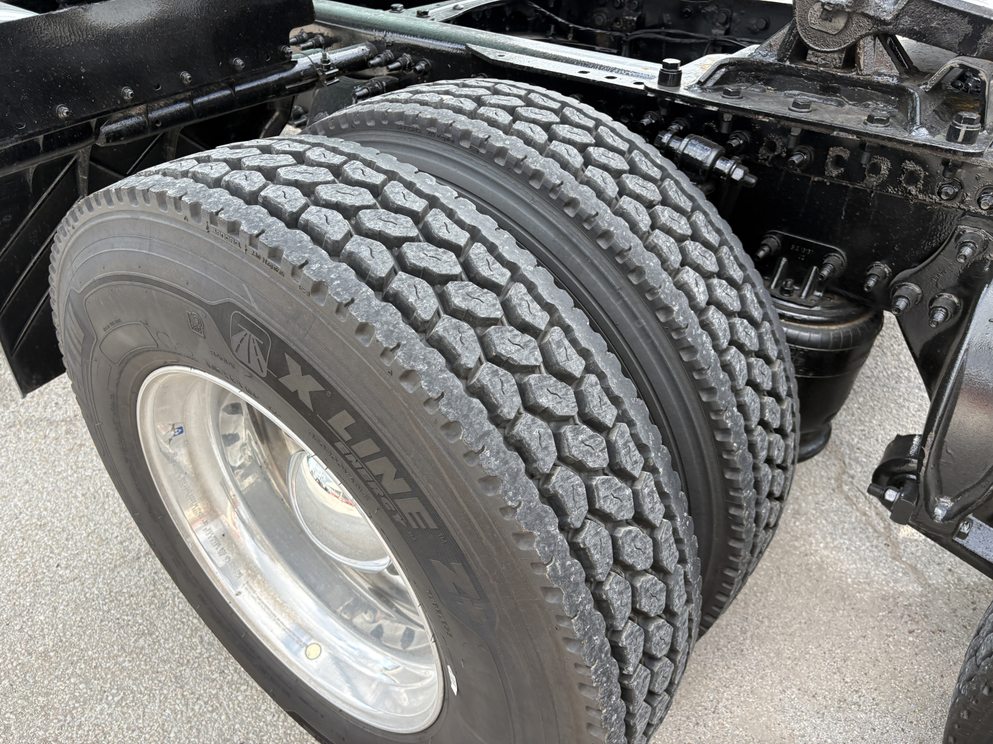 Dual rear truck tires with tread pattern visible, wheel rim, and suspension components of a Freightliner Cascadia 126 chassis.