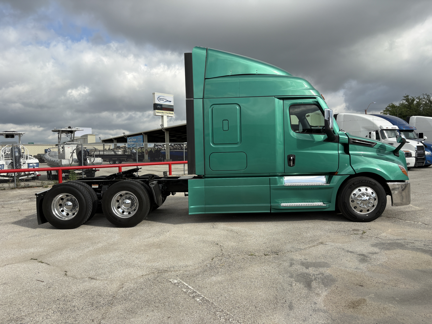 Vehicle side profile of a green Freightliner Cascadia 126 tractor with a flatbed chassis, in-service condition, showing cab and tandem rear axles.