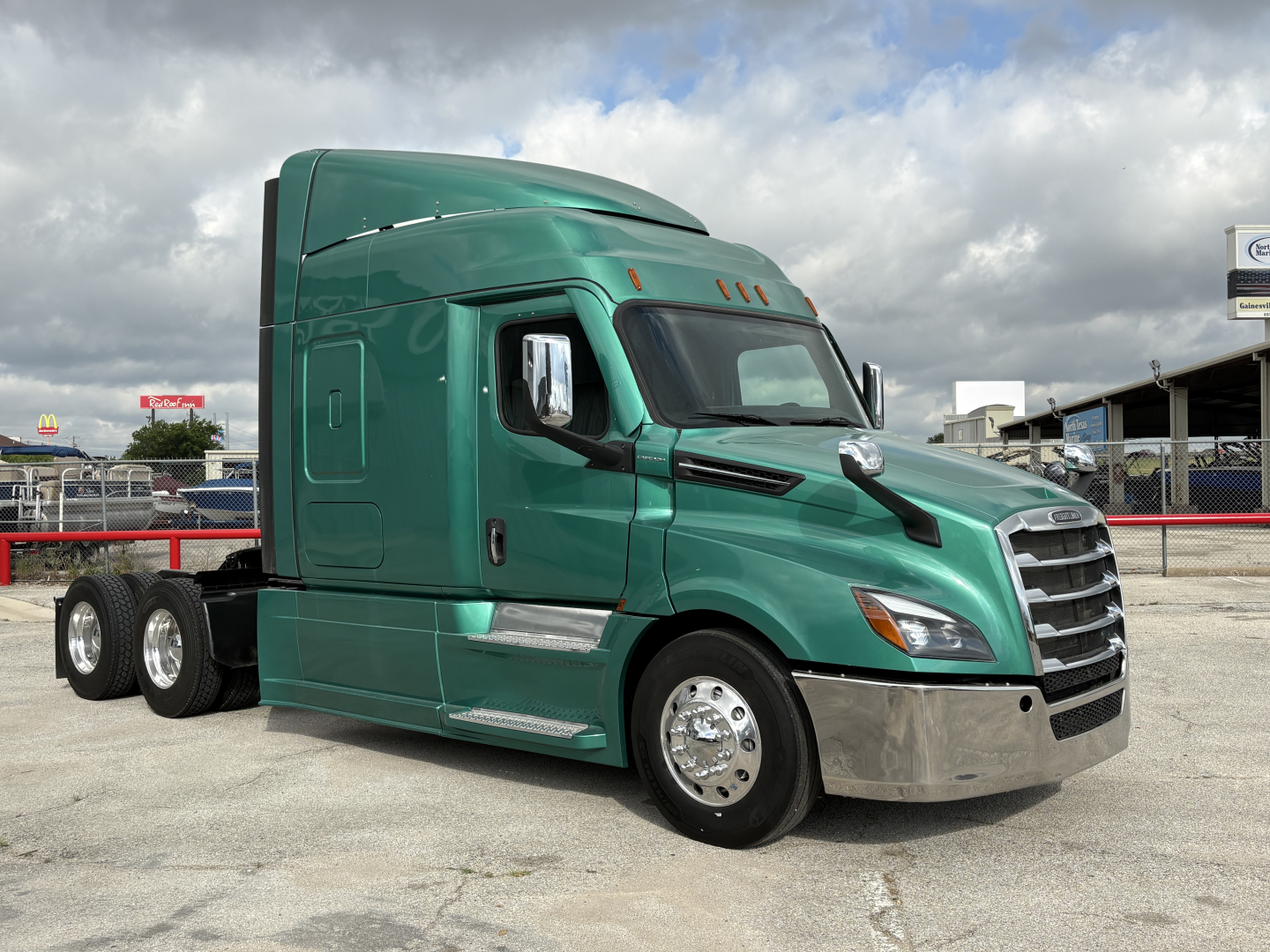 Freightliner Cascadia 126 sleeper tractor in green, side view, front grille, chrome bumper, dual rear axles, daytime with cloudy sky.