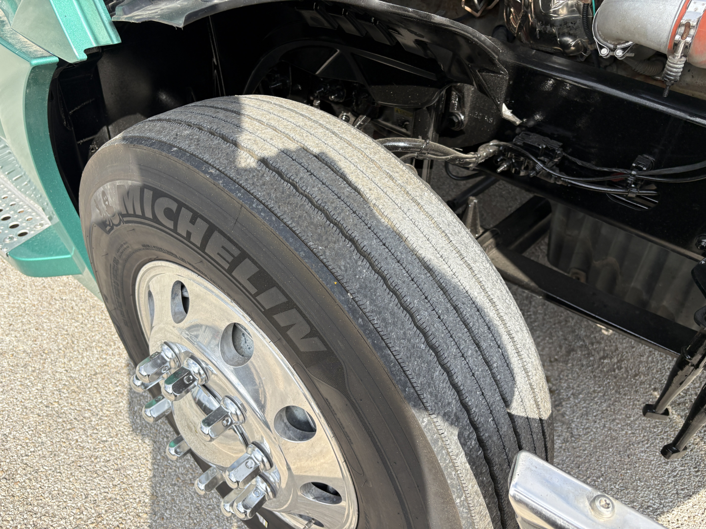 Michelin tire and front suspension area of a Freightliner Cascadia 126 tractor with visible wheel, tire, and part of the engine bay.