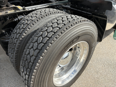 Front dual rear axle tire of a Freightliner Cascadia 126 with tread pattern and polished wheel visible; undercarriage components and part of fender.