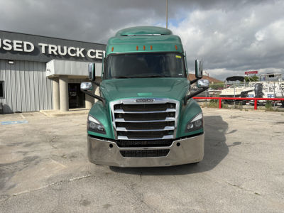 Truck front view of a green 2023 Freightliner Cascadia 126 with chrome grille and bumper, windshield, side mirrors, and cab roof fairing.