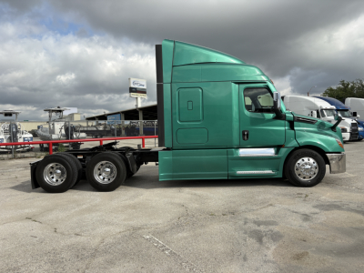 Vehicle side profile of a green Freightliner Cascadia 126 tractor with a flatbed chassis, in-service condition, showing cab and tandem rear axles.