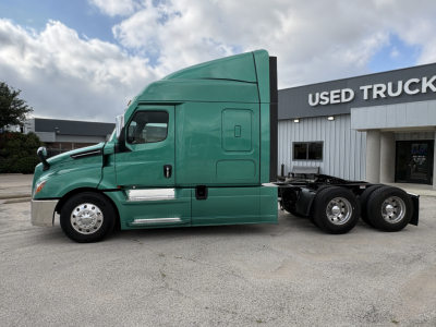 Green Freightliner Cascadia 126 semi-truck tractor in a used truck lot with building in background.