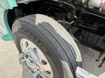 Michelin tire and front suspension area of a Freightliner Cascadia 126 tractor with visible wheel, tire, and part of the engine bay.