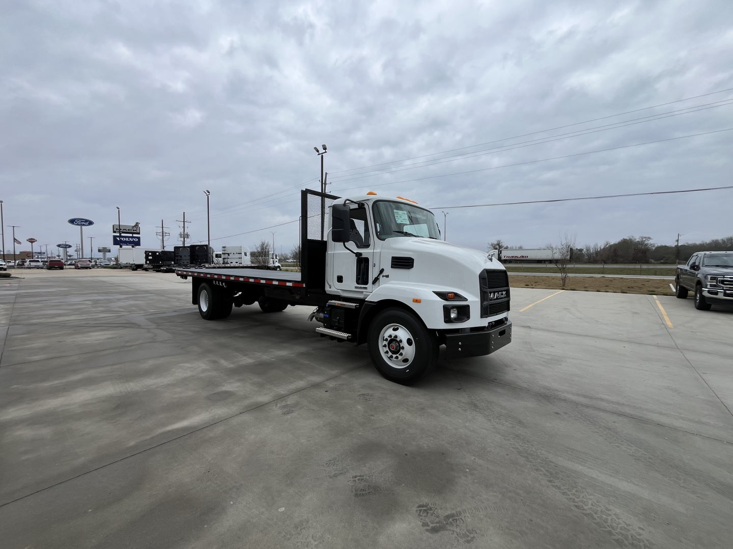 Flatbed tow truck likely a Mack MD6 with a white cab and extended black flatbed, dual rear axles, side steps, and chrome bumper.