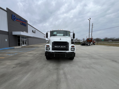 Truck front view of a white Mack MD6 flatbed truck in a dealership lot.