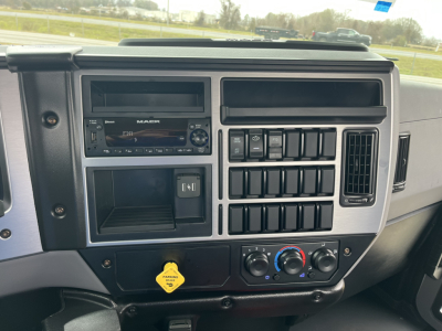 Mack MD6 truck dash showing audio/navigation unit and climate controls with numerous rectangular buttons, gear shifter area, and yellow key tag.