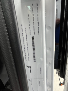 Mack MD6 chassis label/ID plate visible with VIN and barcode data, mounted on door frame area.