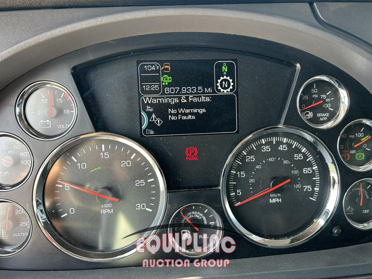 Dashboard of a Kenworth truck showing multiple gauges and a central screen with warnings: ‘No Warnings No Faults’, digital readout 104°F, 1225, 607.933.5 MI, parked indicator, and a red parking brake symbol.