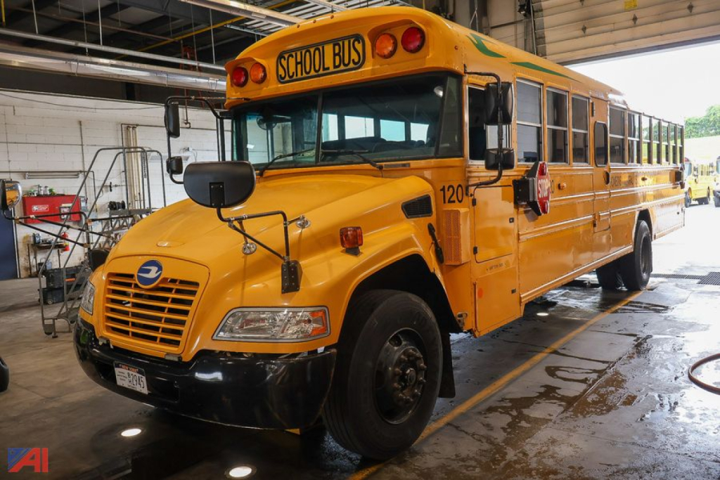 School bus with yellow body and black bumper, emergency lights, and 'SCHOOL BUS' sign on the front; number 120 on the door area; blue Bird emblem on grille.
