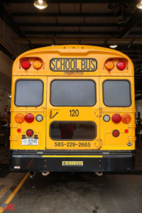 Rear view of a yellow school bus with 'SCHOOL BUS' sign, route number 120, phone number, and Blue Bird logo.