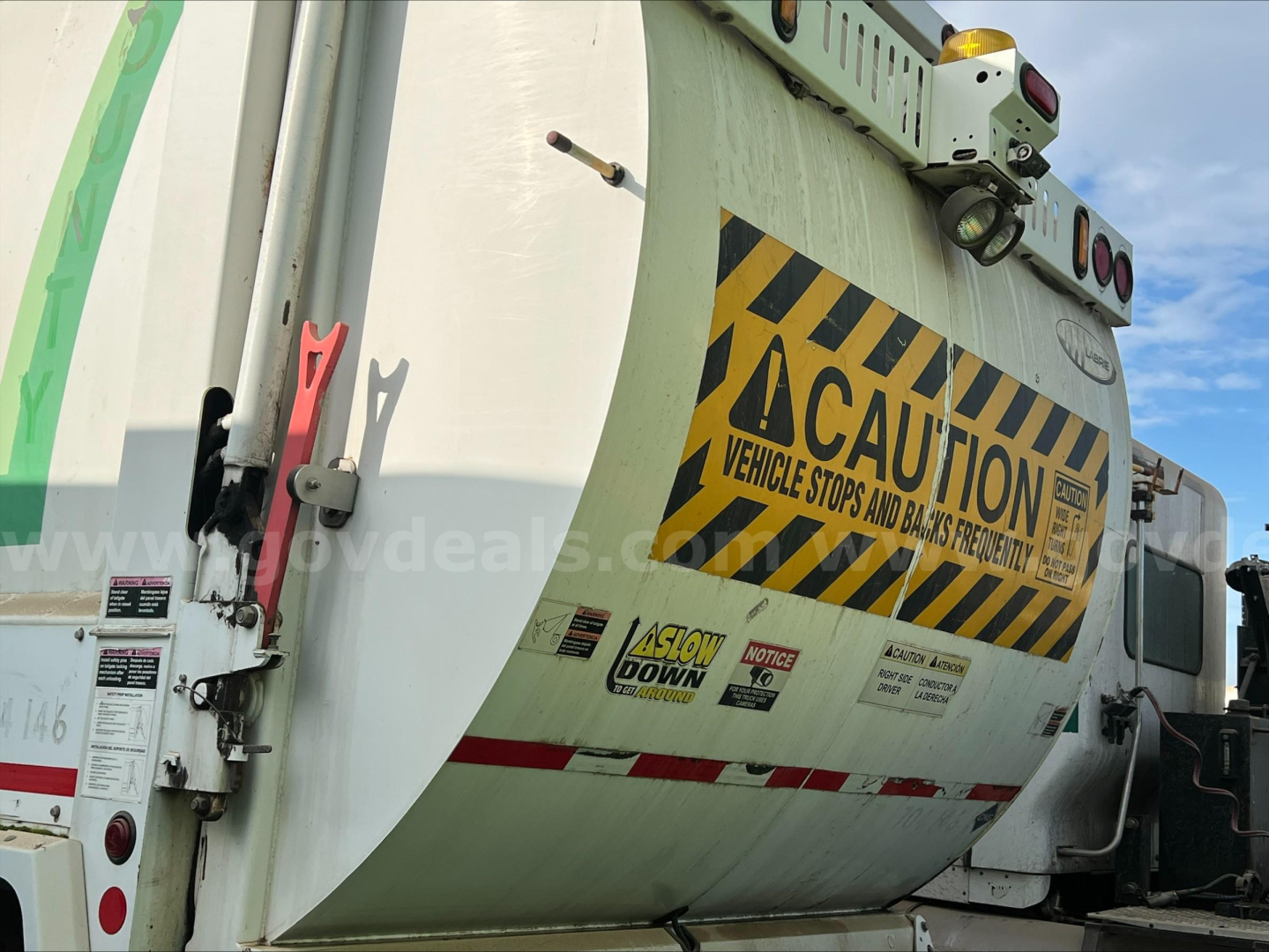 Truck rear showing caution labels and reflective stripes on a garbage truck body.