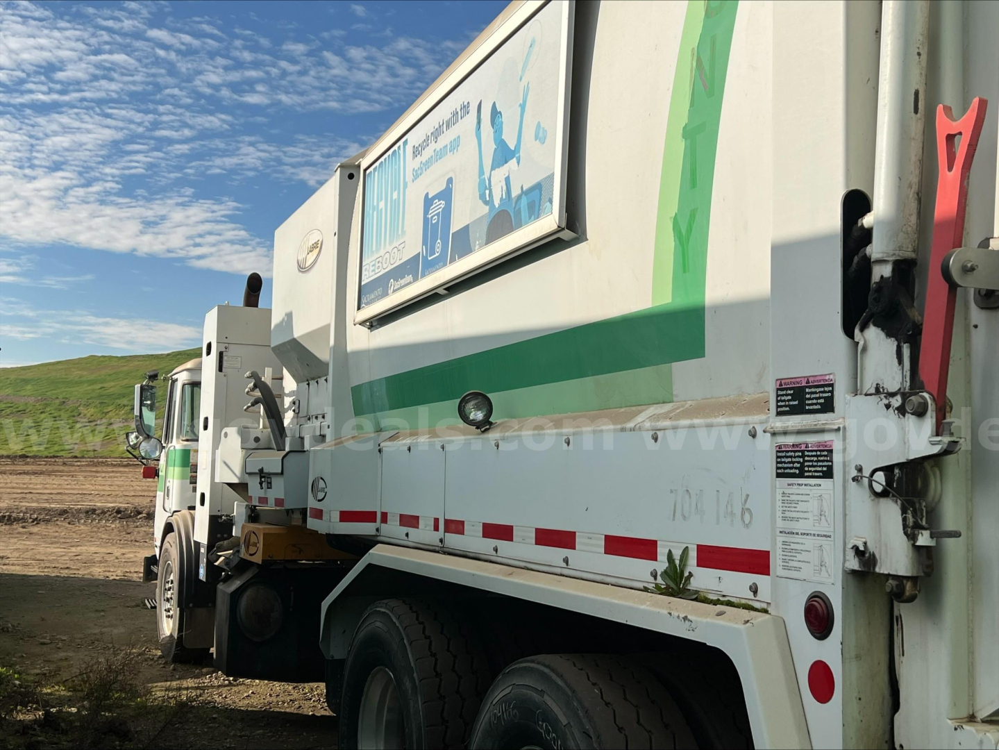 Autocar ACX XPeditor waste collection truck side view showing rear hopper with green decal and safety stickers.