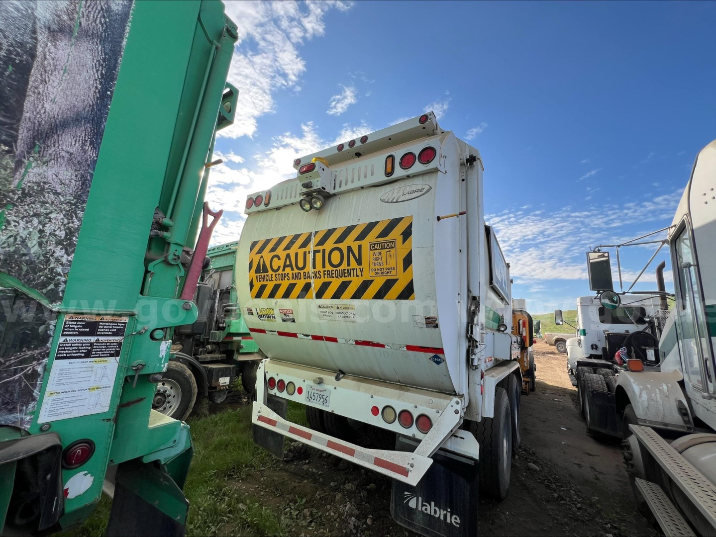 Truck dump body with hazard caution label and rear lights visible in a yard.