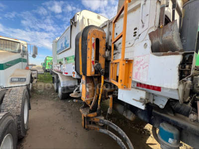 Autocar ACX XPeditor truck in yard showing large orange hydraulic arm and rear equipment, side of chassis, other trucks in background.