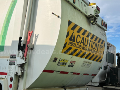 Truck rear showing caution labels and reflective stripes on a garbage truck body.