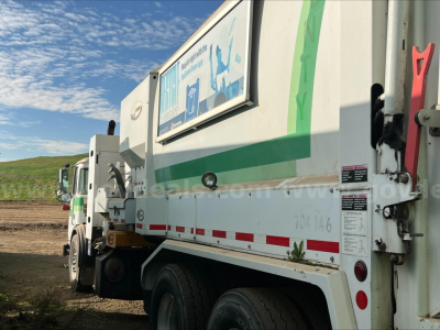 Autocar ACX XPeditor waste collection truck side view showing rear hopper with green decal and safety stickers.