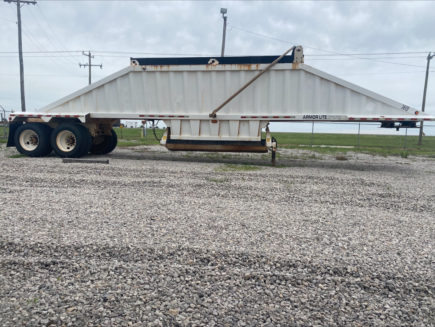 Trailer side view of a white Armor Lite SBD40 dump trailer with a double-axle rear, showing the long flatbed undercarriage and branding 'Armor Lite' near the front.