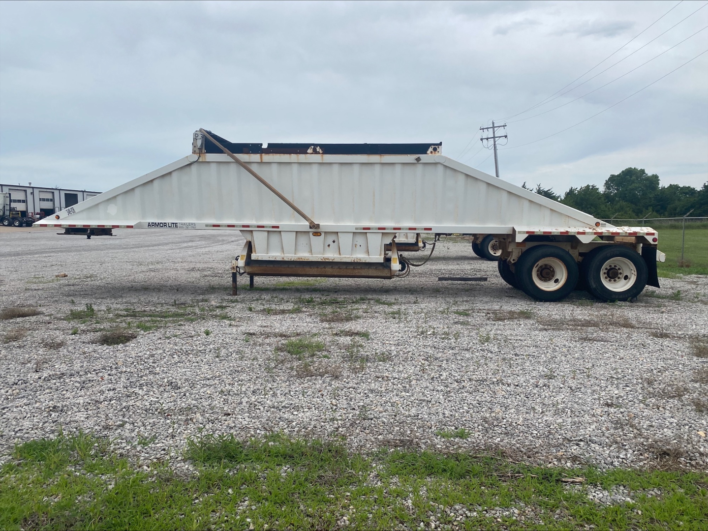 Dump trailer in side view showing Armor Lite SBD40 skeleton dumping trailer with dual rear axles and white-gray body.