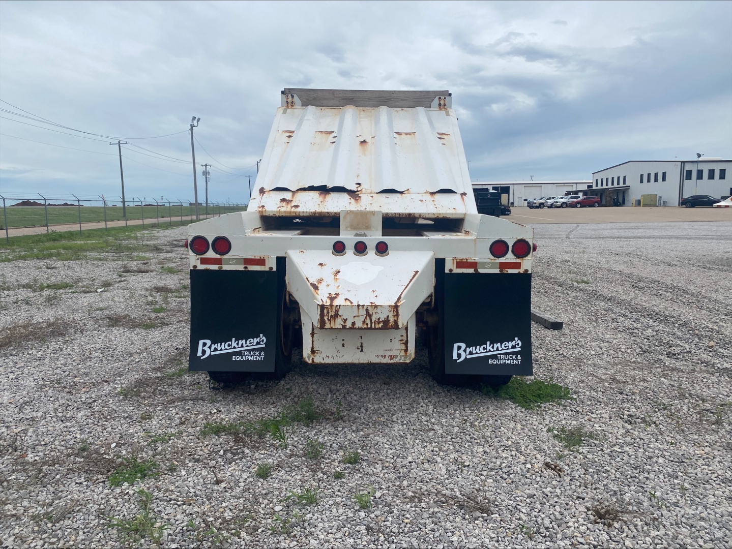 Dump trailer rear view showing Armor Lite SBD40 skeleton dump with rust on hopper and taillights, Bruckner’s mud flaps, gravel lot.