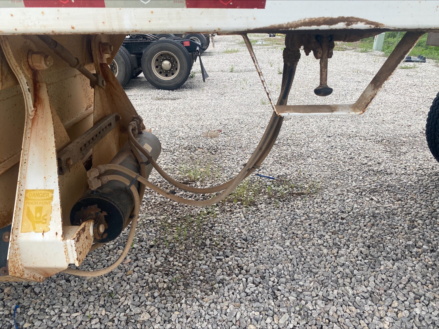 Trailer undercarriage showing hoses and connector fittings on Armor Lite SBD40 skeleton dump trailer, gravel surface, VIN tag area visible.