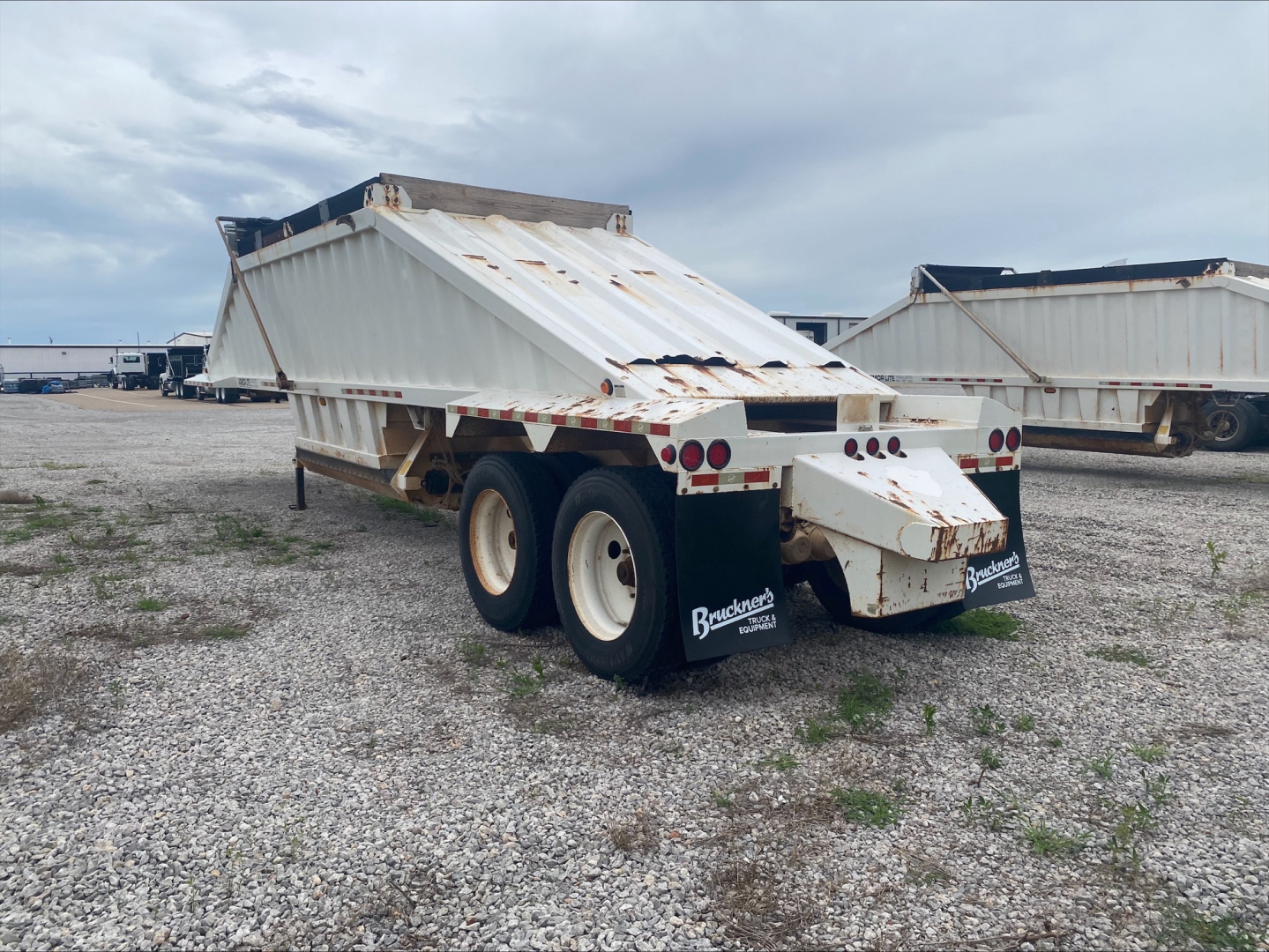 Dump trailer showing white Armor Lite SBD40 skeleton bed with dual rear axles and mud flaps.