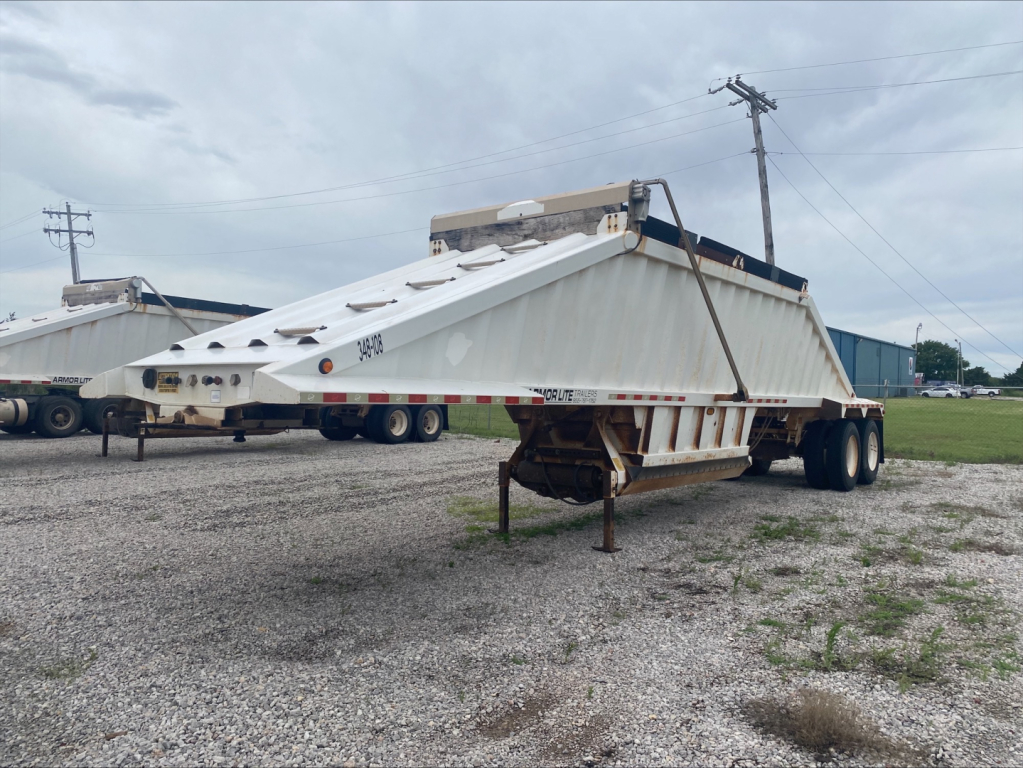 Dump trailer showing Armor Lite SBD40 skeleton design with white body and dual rear axles, raised hopper, and front hitch area visible.