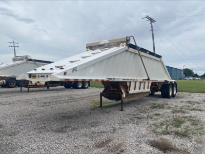 Dump trailer showing Armor Lite SBD40 skeleton design with white body and dual rear axles, raised hopper, and front hitch area visible.
