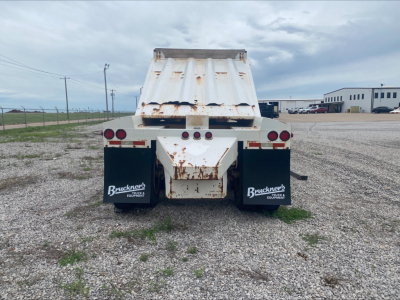 Dump trailer rear view showing Armor Lite SBD40 skeleton dump with rust on hopper and taillights, Bruckner’s mud flaps, gravel lot.