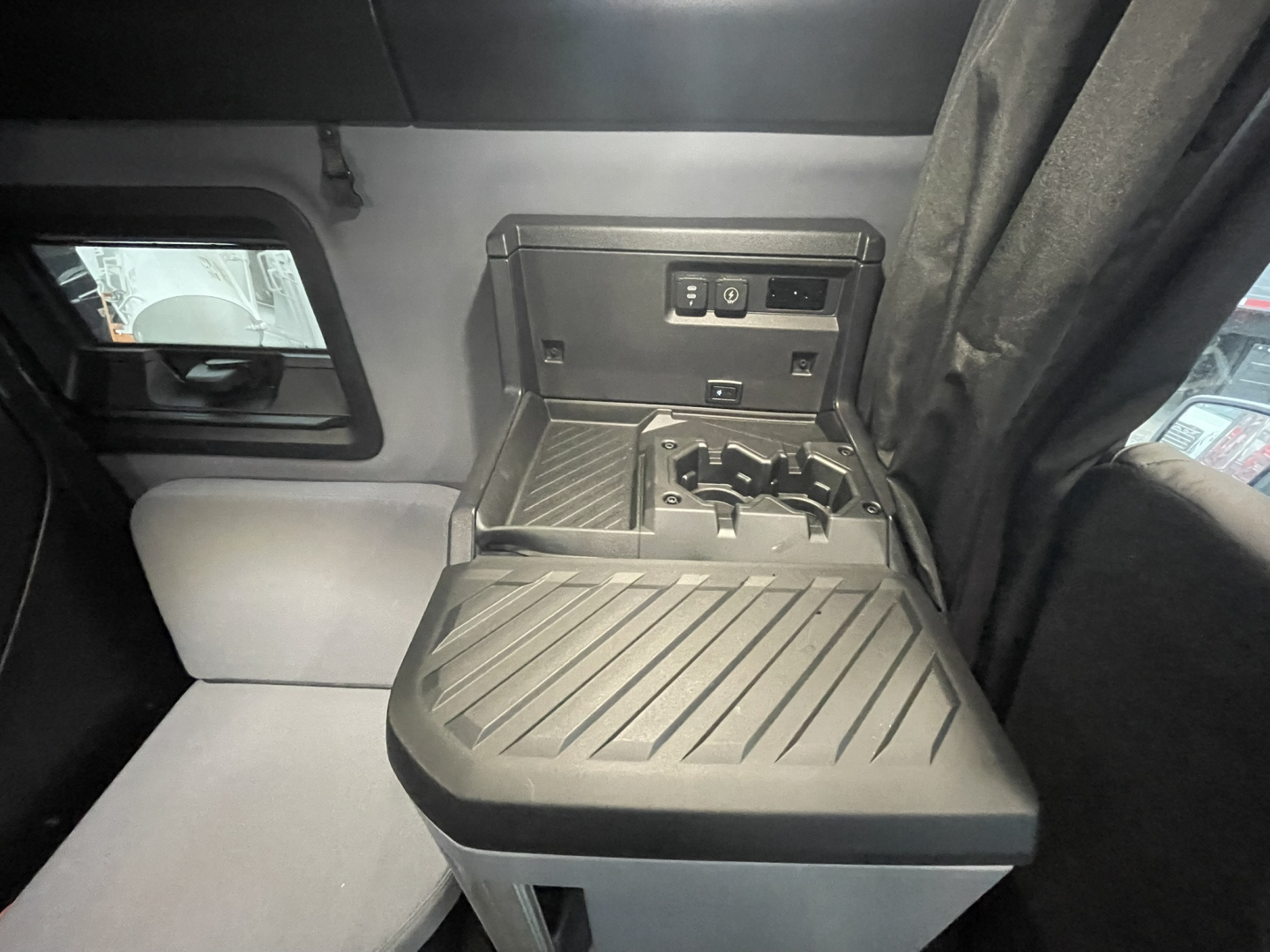 Interior of a Mack PR64T76H sleeper cab showing center console with cup holders and controls, dash area, and window view.