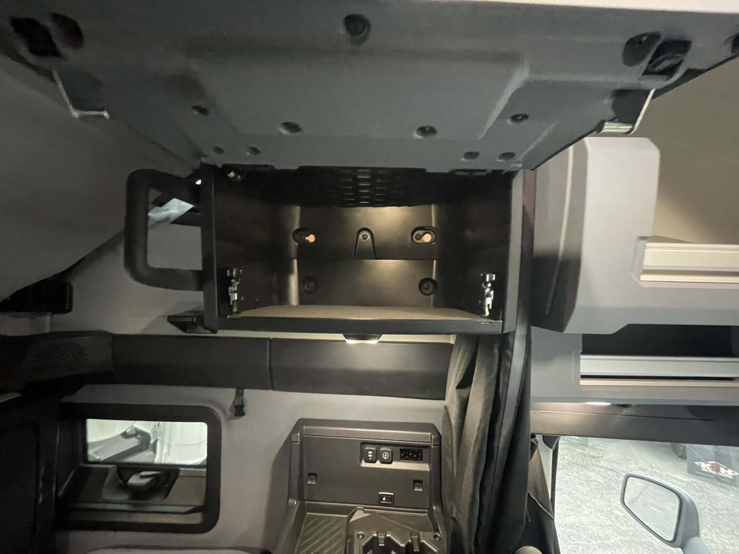 Interior view of a 2026 Mack PR64T76H cab area showing under-dash storage area and panels with mounting brackets.