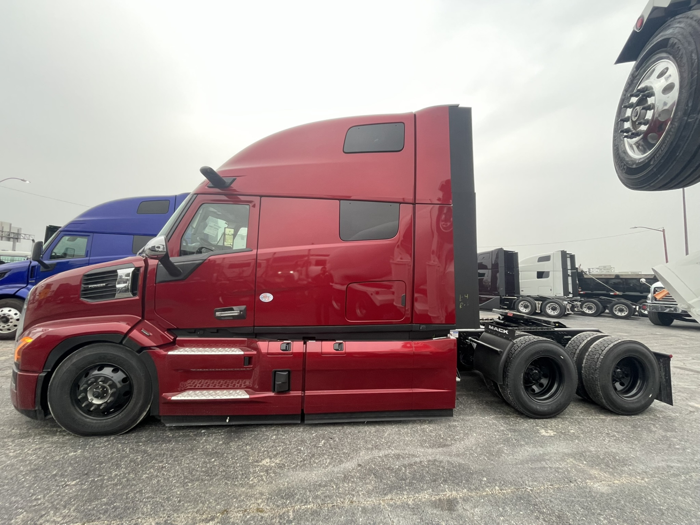 Truck side profile showing a red Mack PR64T76H tractor with a tall sleeper cab, black chassis, and dual rear axles. Visible text on side panels includes Mack branding and model details.