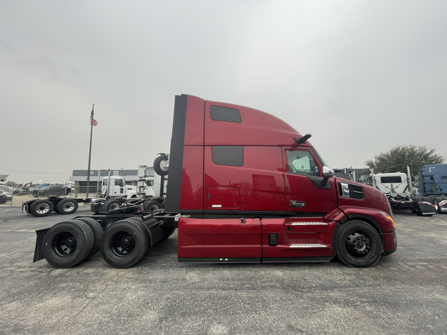 Truck side view of a red Mack PR64T76H conventional sleeper tractor, 6x4 with three rear axles, showing cab, fuel tanks, and wheels.