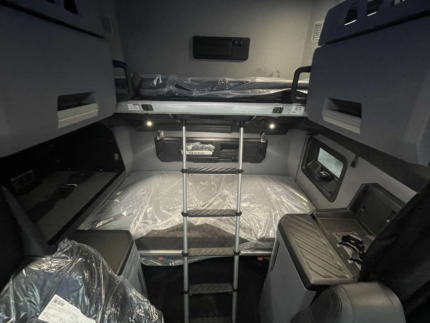 Mack PR64T76H sleeper cab interior showing top bunk bed with ladder and surrounding storage compartments.