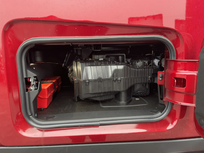 Truck cab storage door open showing diesel engine/air intake area with battery pack visible inside compartment