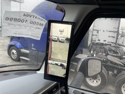 Truck cab interior showing a vertical touchscreen display mounted near the windshield with side mirrors and other trucks visible outside.