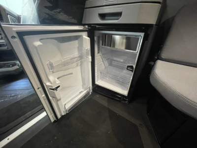 Mack PR64T76H truck cab interior showing a small under-dash refrigerator/freezer unit with white interior shelves and door compartments.
