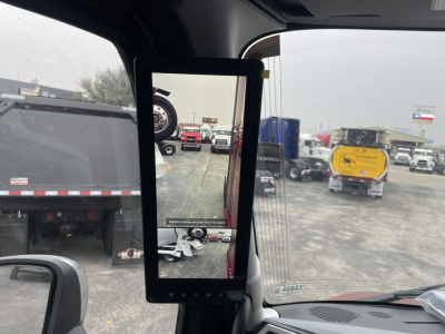 Mack PR64T76H truck cab interior with side mirror and a rearview monitor showing a truck yard.
