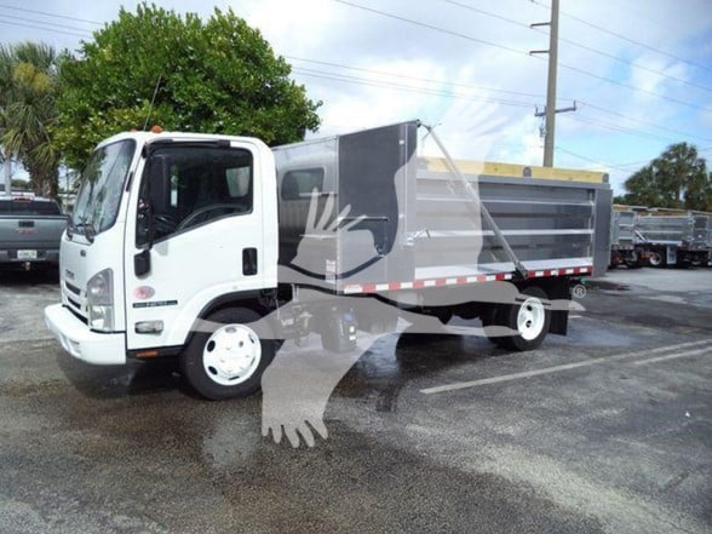 Diverging Isuzu NPR XD dump truck in-service showing side dump bed with gray panels and white cab.