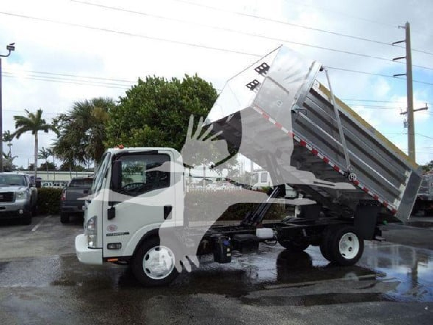 Isuzu NPR XD dump truck in a dealership lot, white cab with tipped silver dump bed, VIN tag not visible, stock number T00823L, used vehicle.