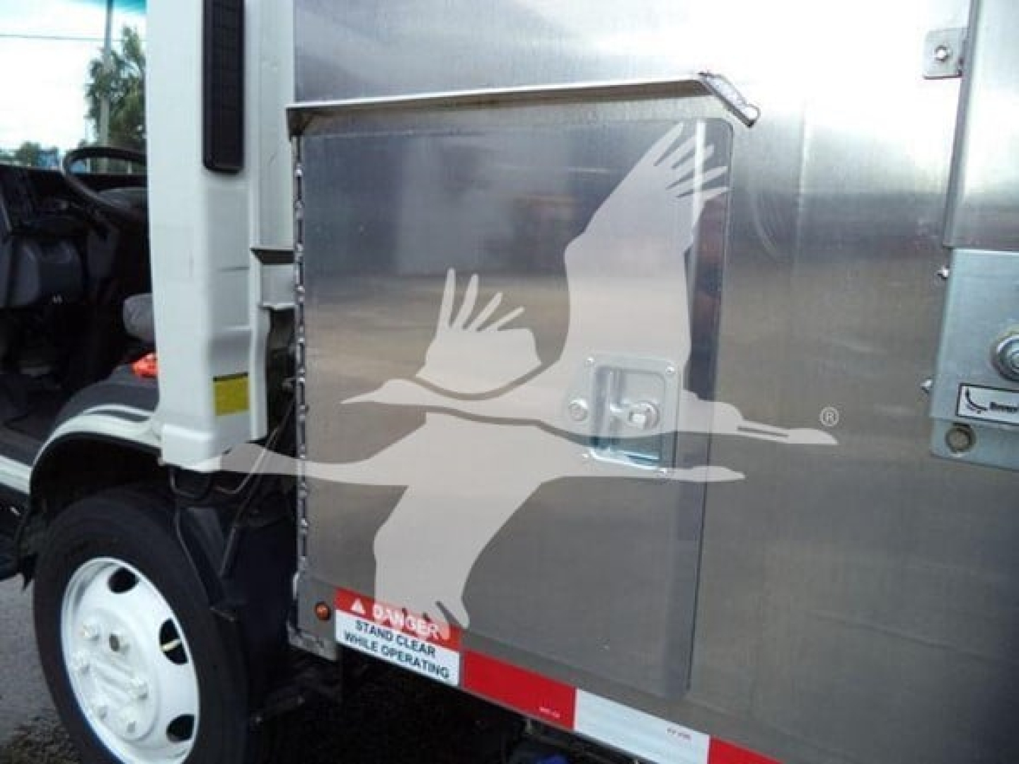 Isuzu NPR XD truck side panel with logo and reflective stripe, aluminum cargo box, front wheel and cab visible.