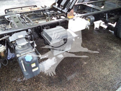 Isuzu NPR XD chassis view showing fuel/water reservoirs and mounting brackets with visible liquid exposure on ground.