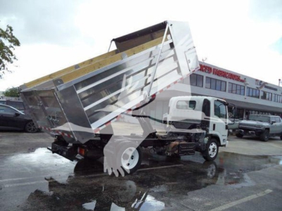 Isuzu NPR XD truck with a lifted dump bed in a dealership lot showing a white cab and metal dump bed.