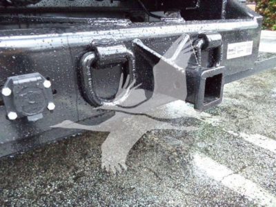 Isuzu NPR XD truck rear bumper area showing hitch receiver, towing eye, and electrical connector with label plate and surrounding surface.