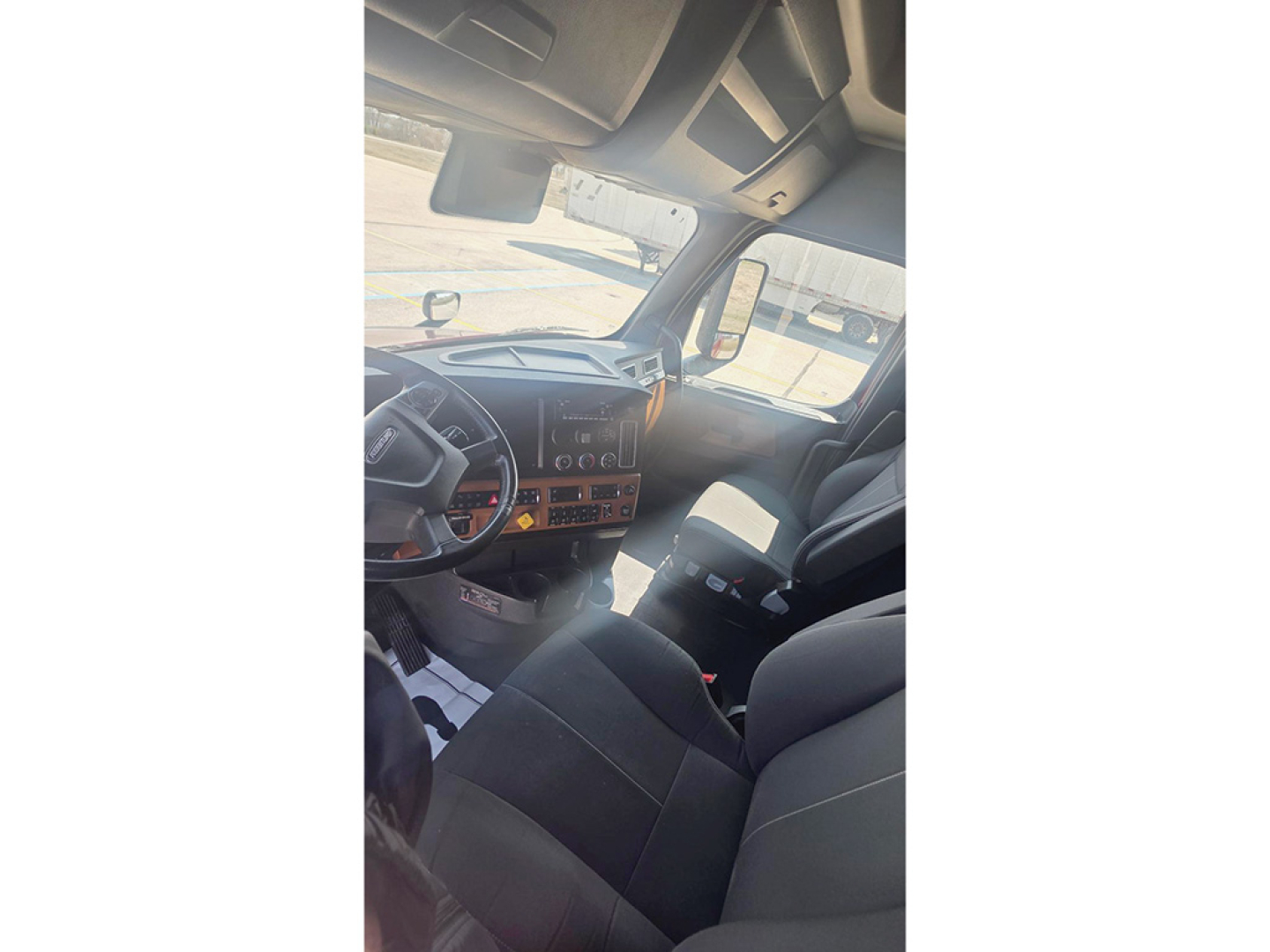 Cab interior of a Freightliner Cascadia126 truck showing dashboard with wood-tone trim, steering wheel, and front seats.